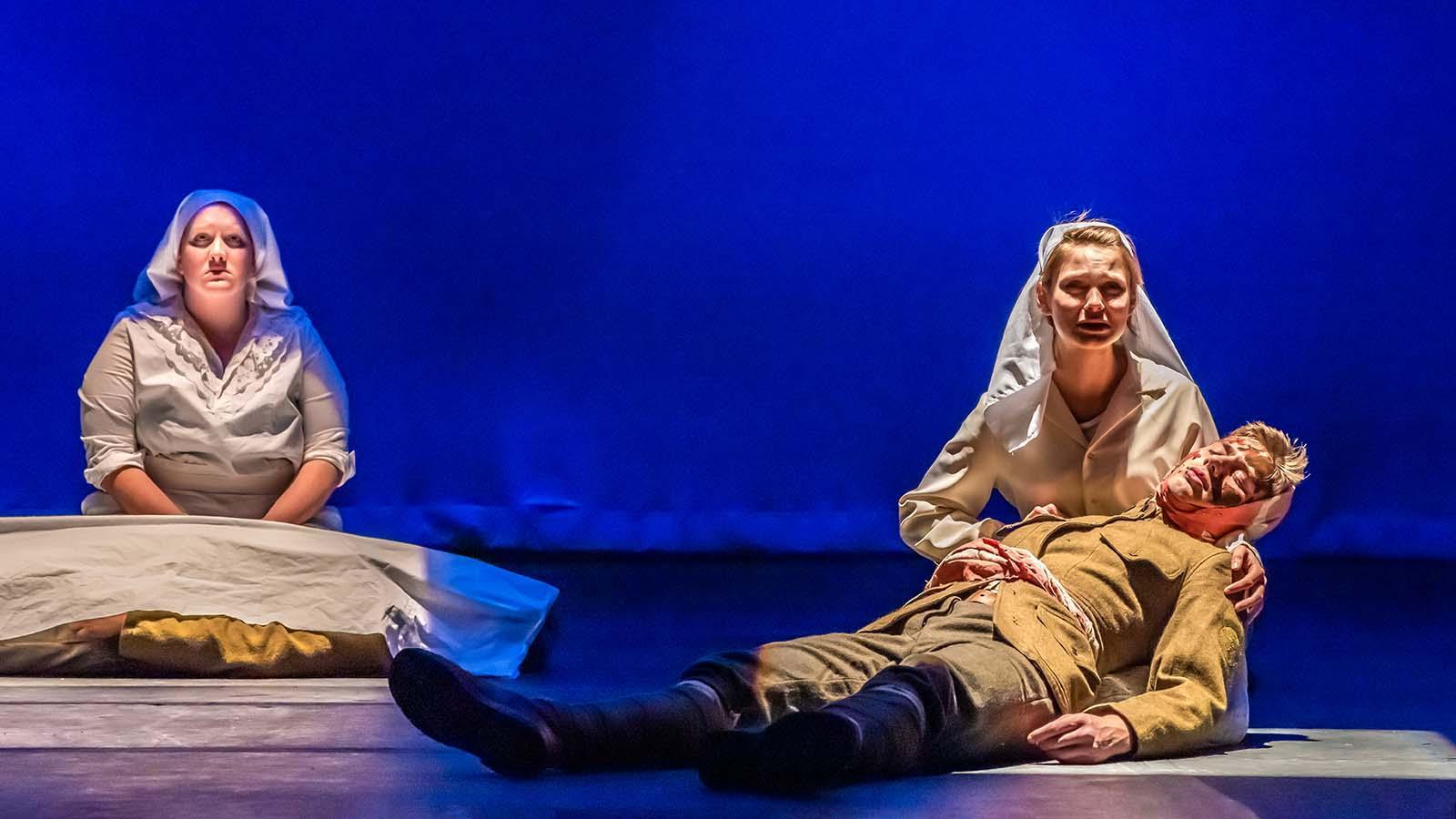 一名学生女演员在舞台上扮演一名一战护士，她跪着抱着一名扮演阵亡士兵的演员. 另一位一战护士坐在他们后面.